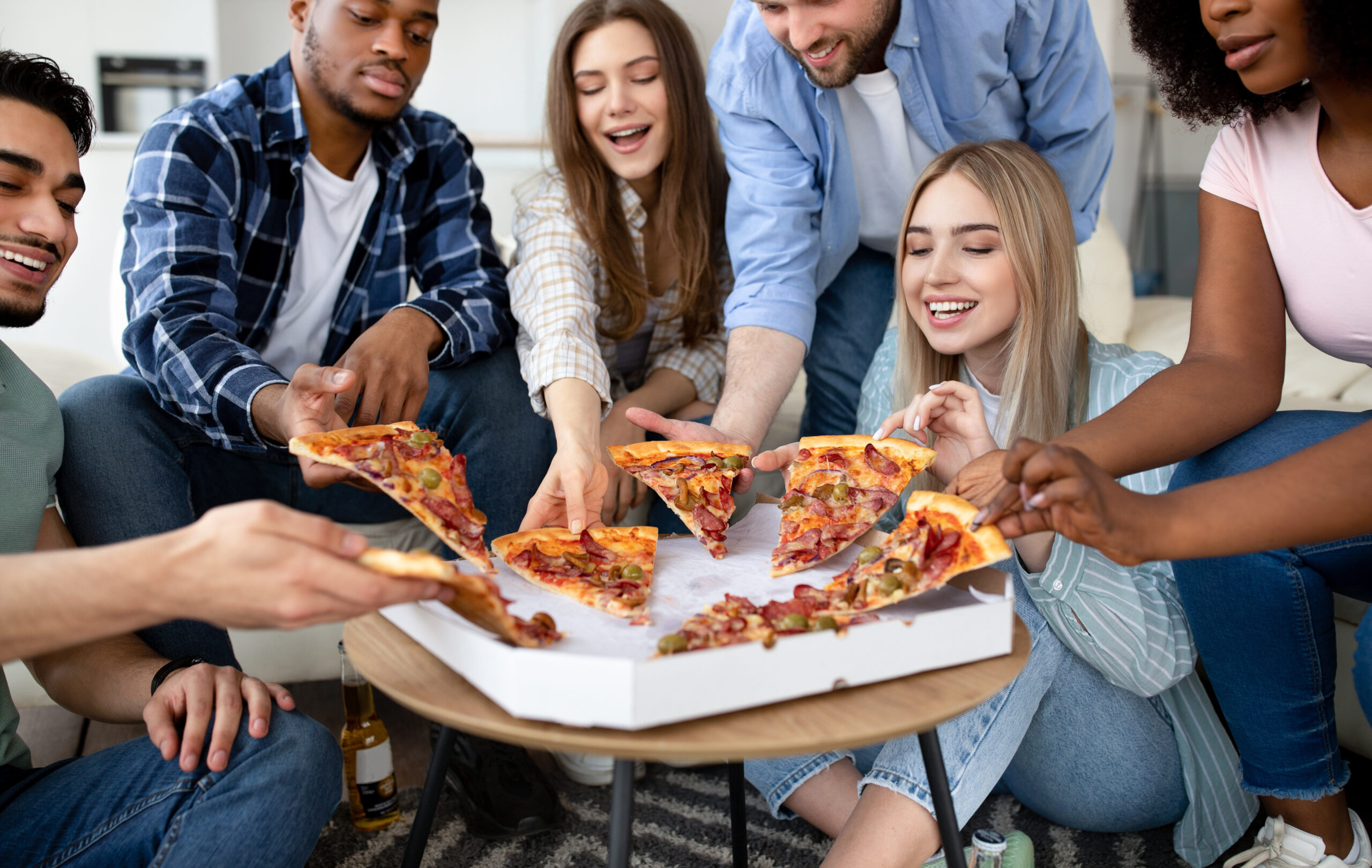 Happy multiracial friends chatting, eating pizza together, having small party at home